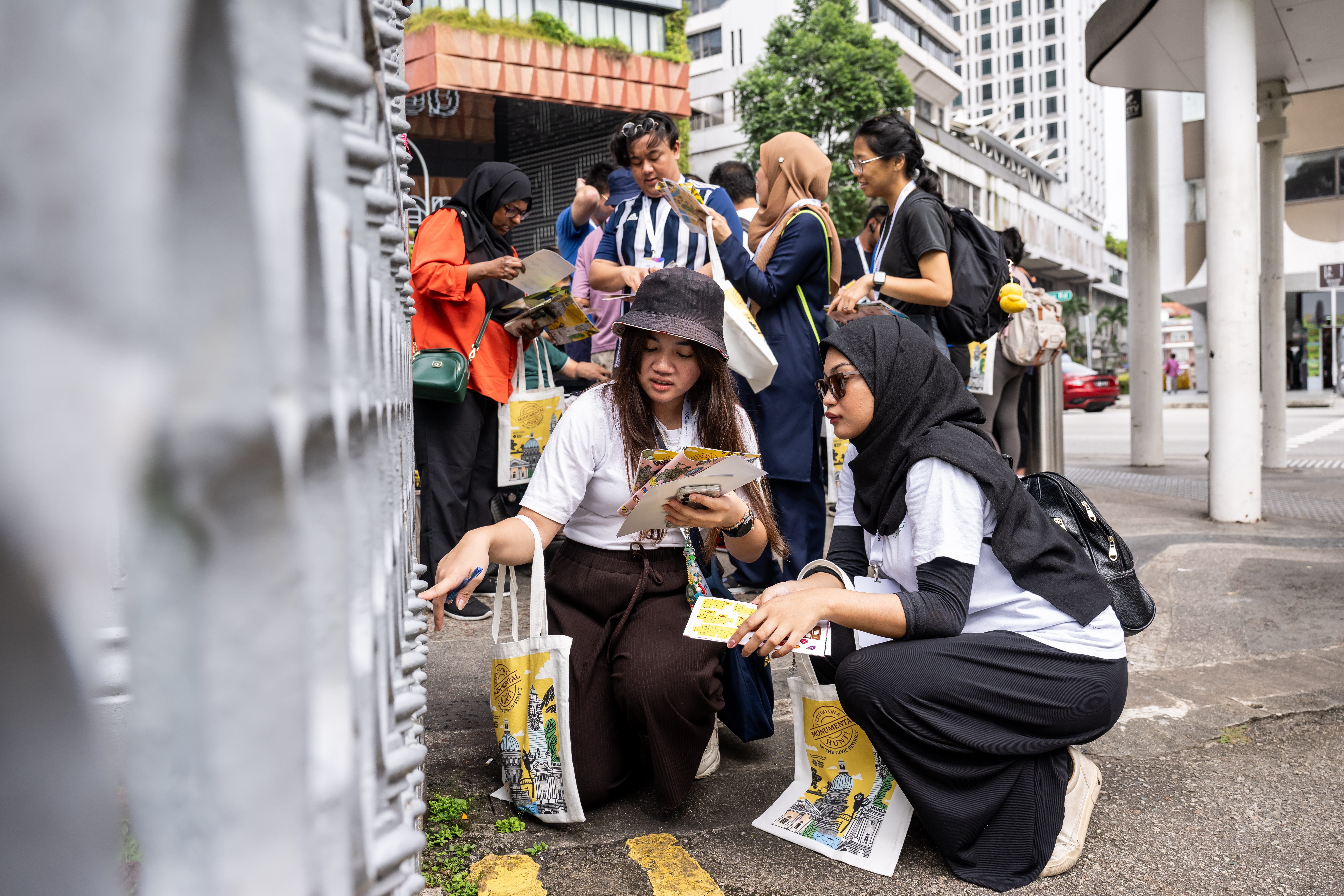 Group of people with tote bags and postcards, carrying out an activity outdoors in City Hall.